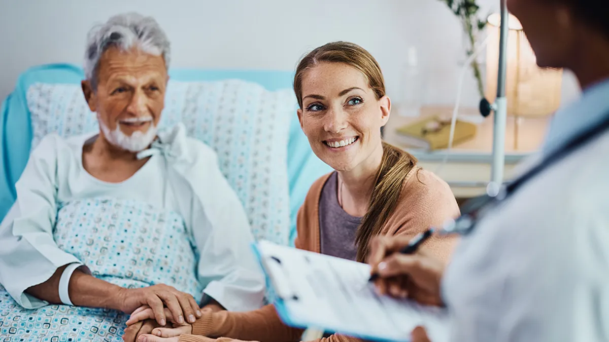 Happy woman and her ill father holding hands while communicating with a doctor in hospital ward.