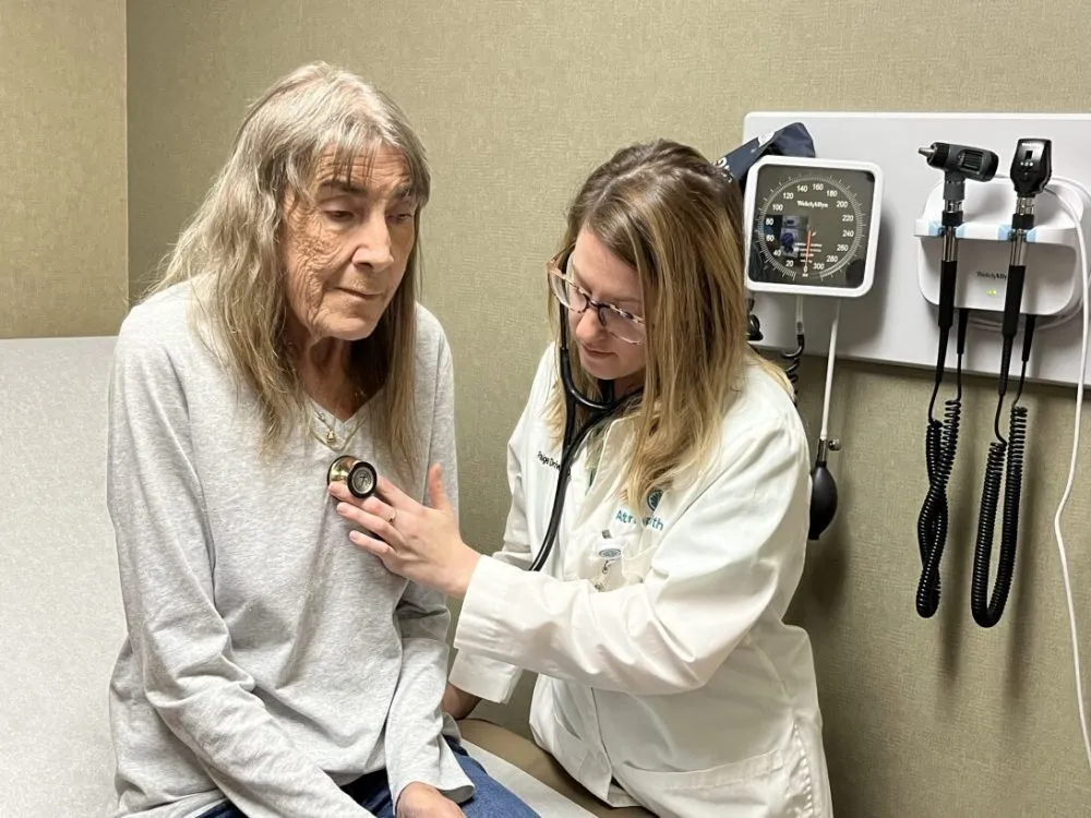 A doctor holds a stethoscope to an elderly patient&#x27;s chest.