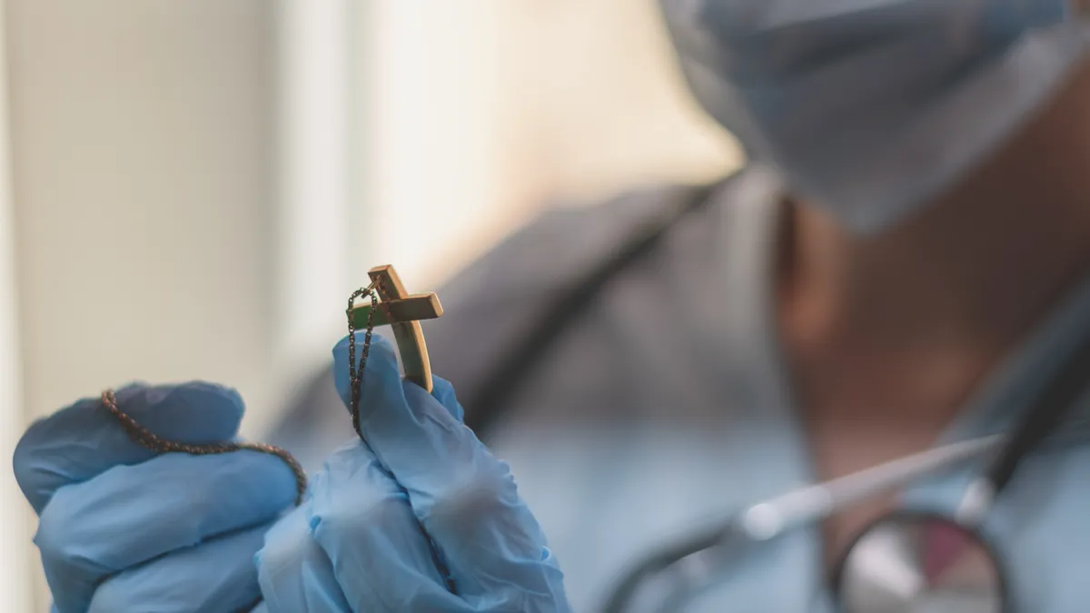 A medical worker in personal protective equipment holds a crucifix.