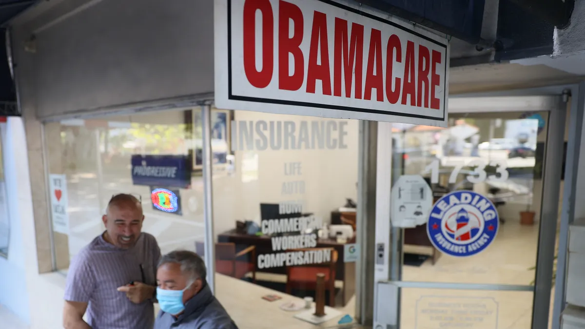 Two men stand on the sidewalk outside of an insurance agency.