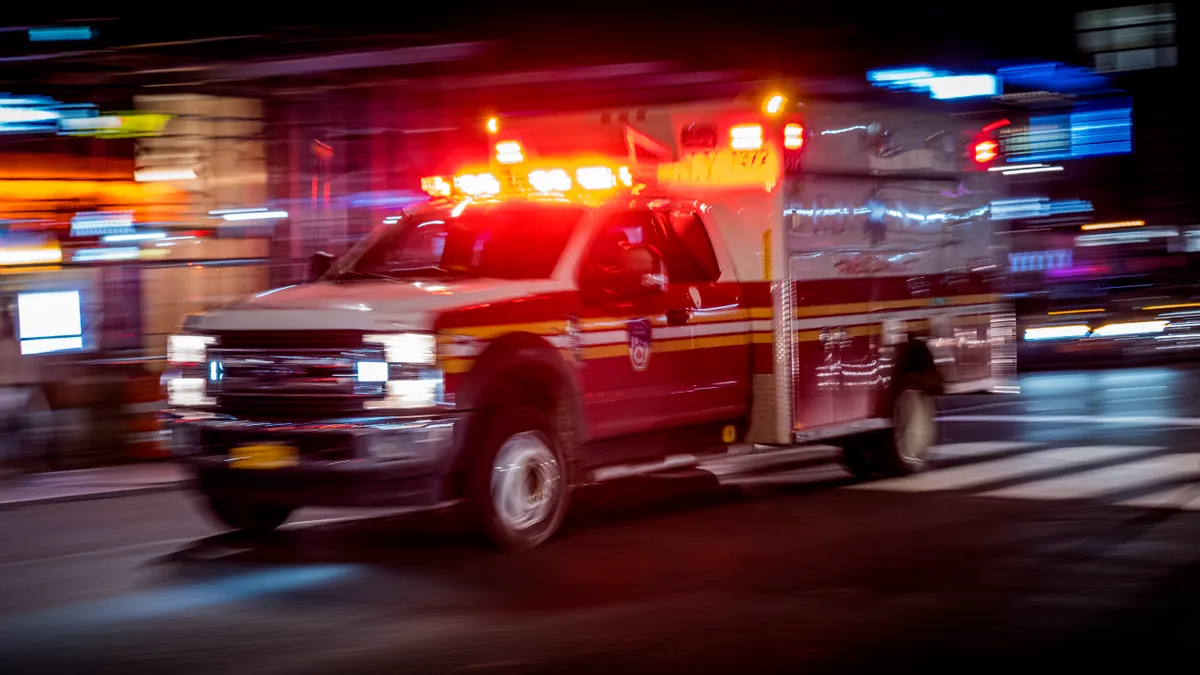 New York Fire Department ambulance with emergency lights on at night driving through an intersection in Midtown Manhattan, blurry due to vehicle in motion