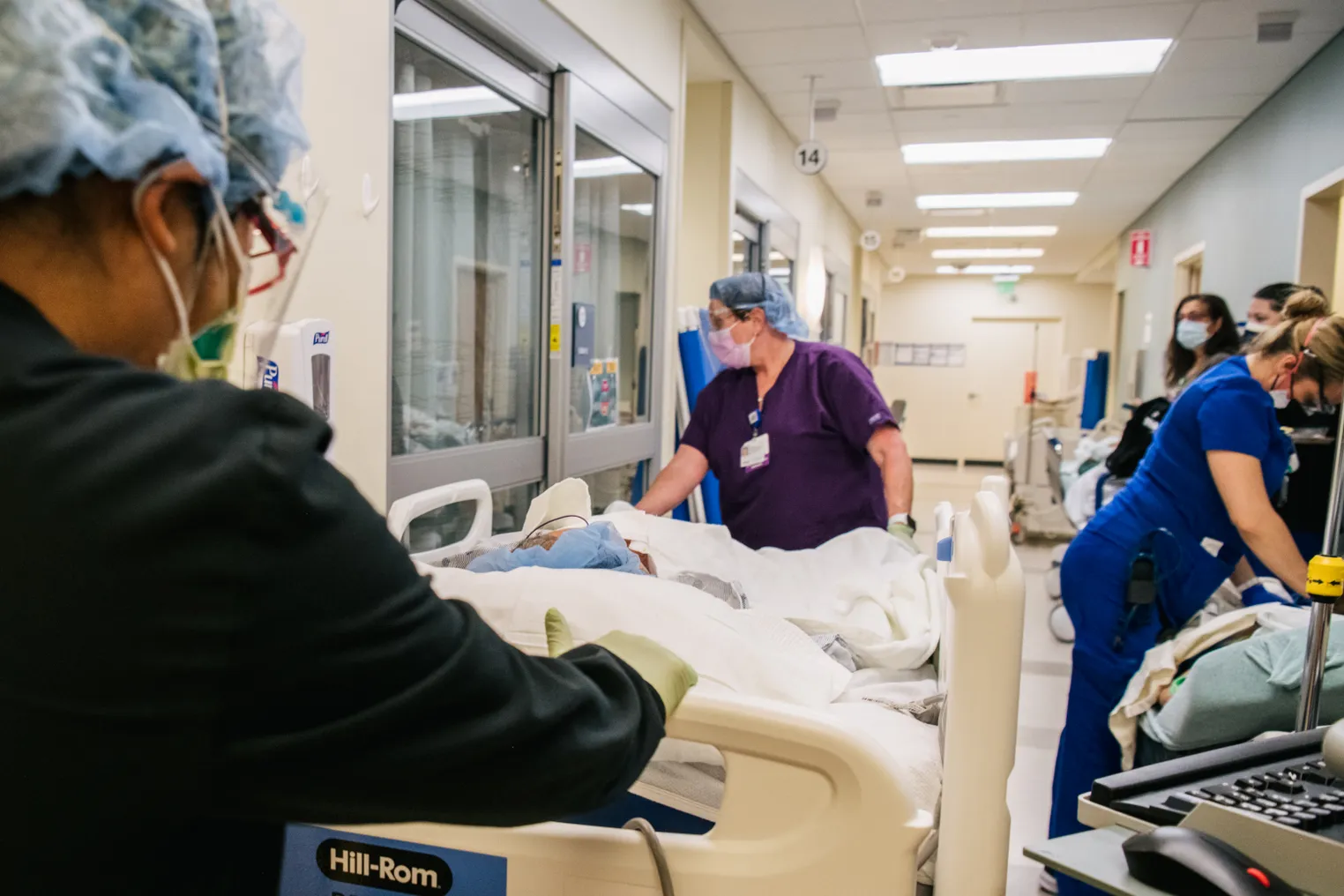 Two emergency room nurses wheel a patient on a gurney through a hospital hallway.