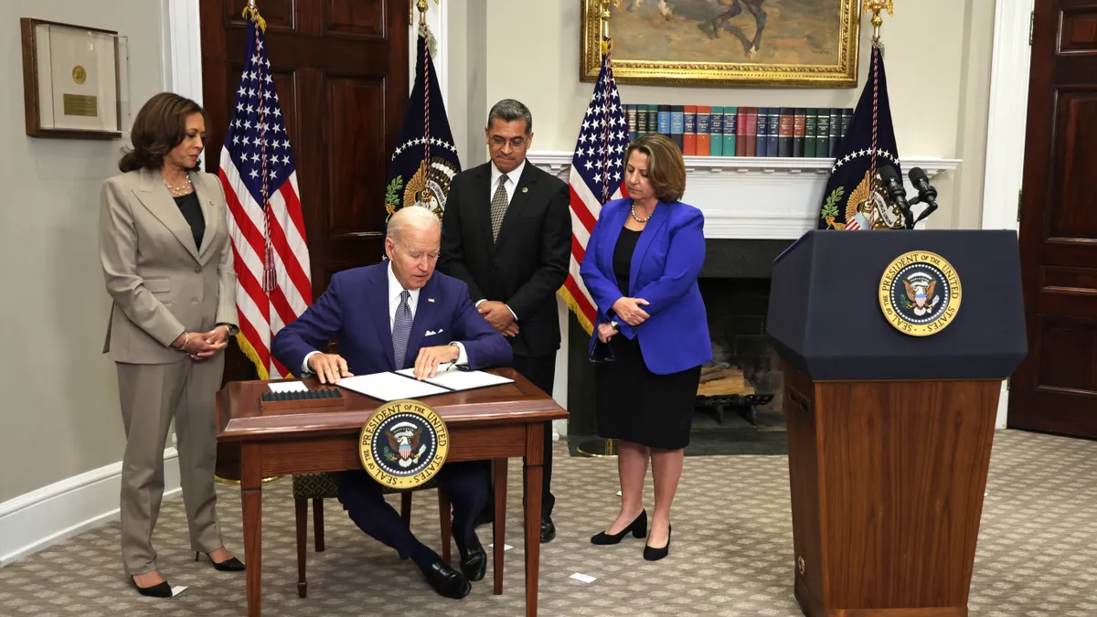 President Joe Biden sits at a desk signing an executive order on reproductive rights as administration officials stand beside him.