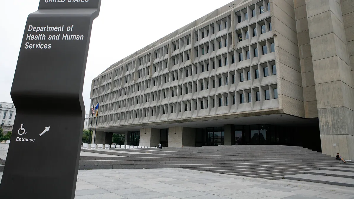 A picture of the exterior of the US Department of Health and Human Services. In front of the building is a black sign designating the building's name.