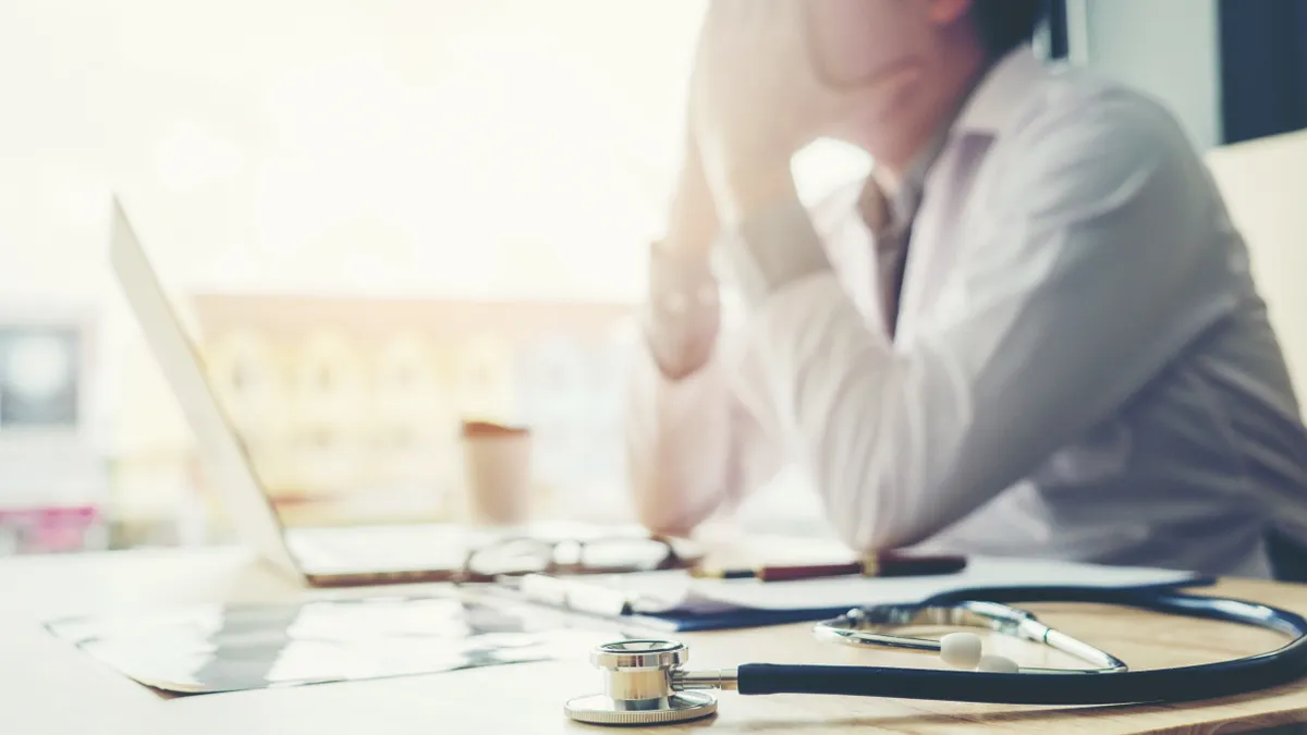 a physician sits at a desk with their head in their hands