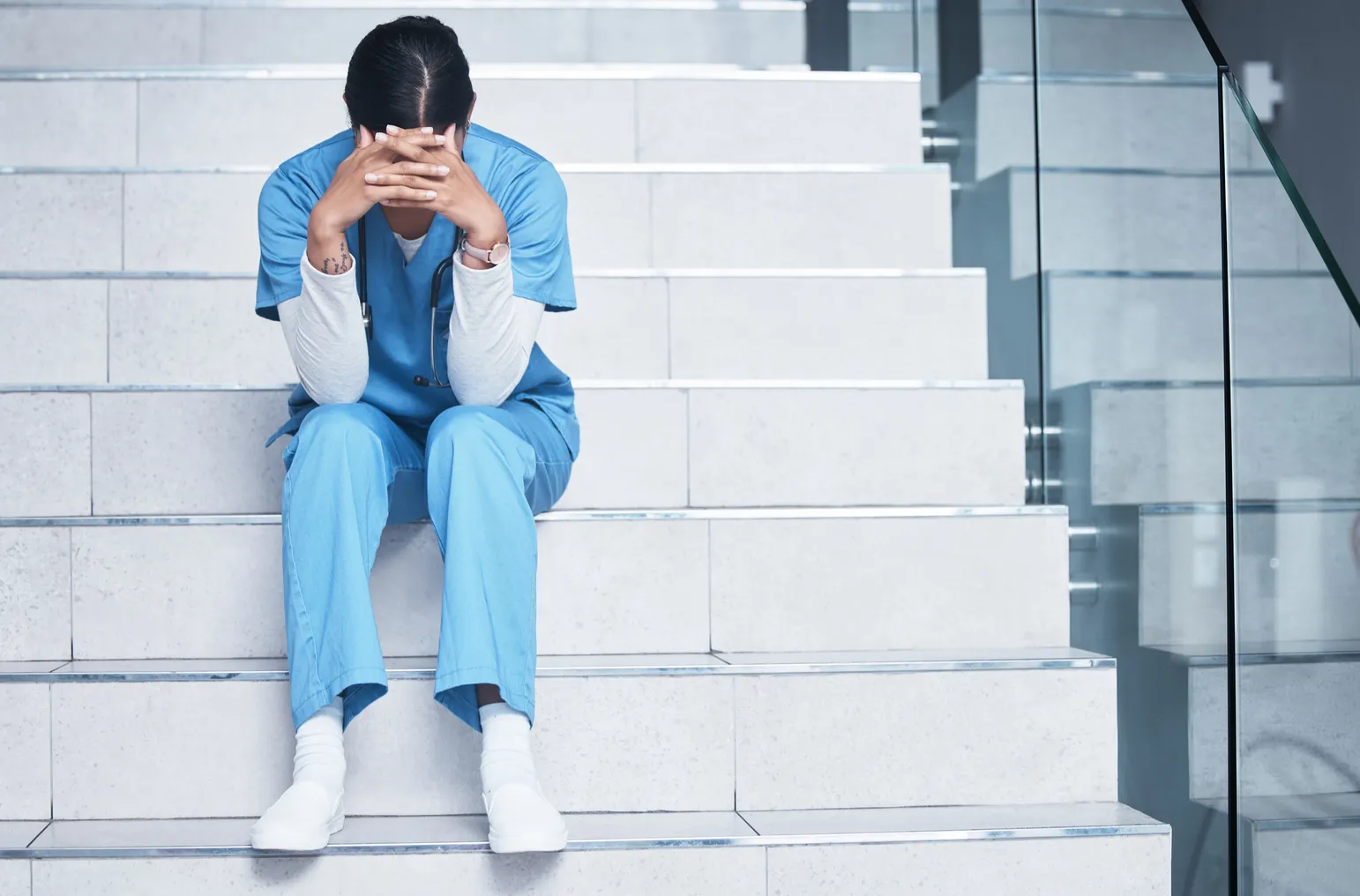 Shot of a female nurse looking stressed while sitting on a staircase stock photo