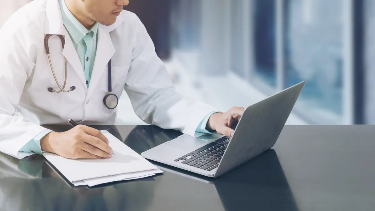 A doctor with a white lab coat looking at a computer on a table full of papers