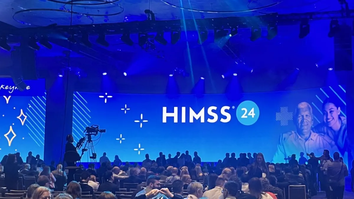 The HIMSS logo is seen on a massive screen onstage in front of a crowd of people.